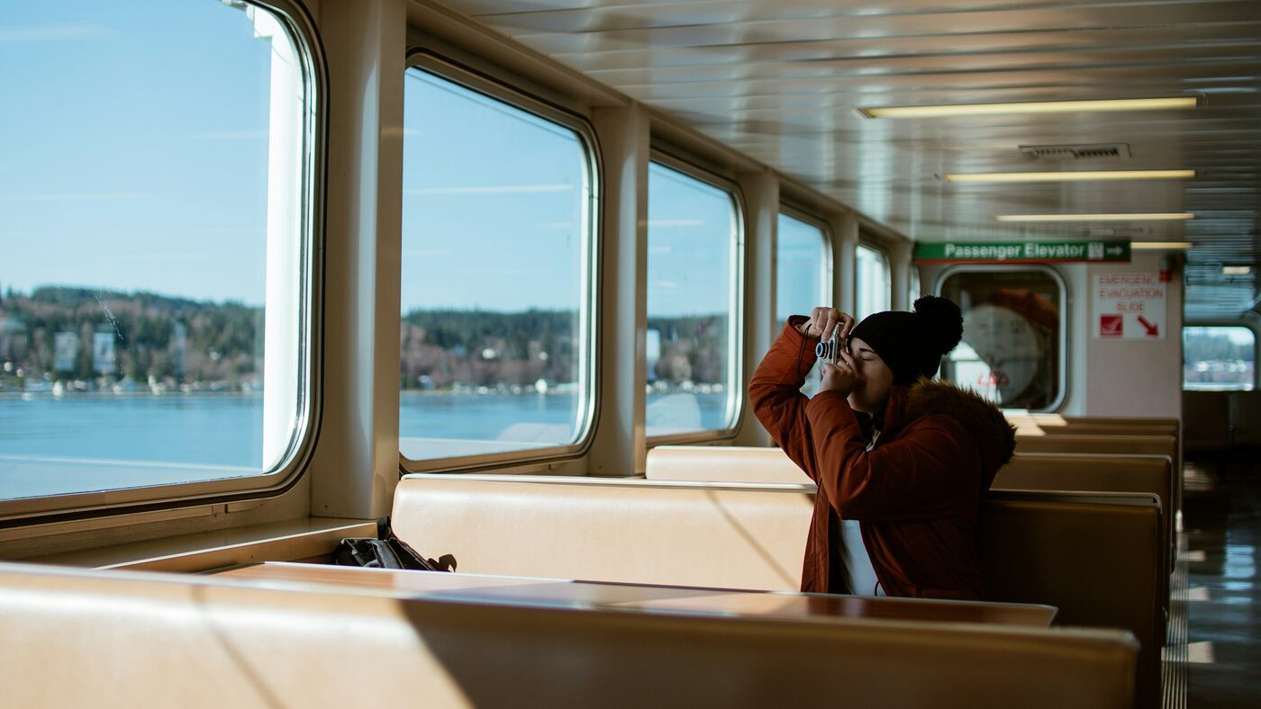 A person alone on a ferry, photographing the coastline through the window